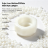 Injection molded white hex nut sample with plastic pellets, showing the hex body and central bore for fastening parts