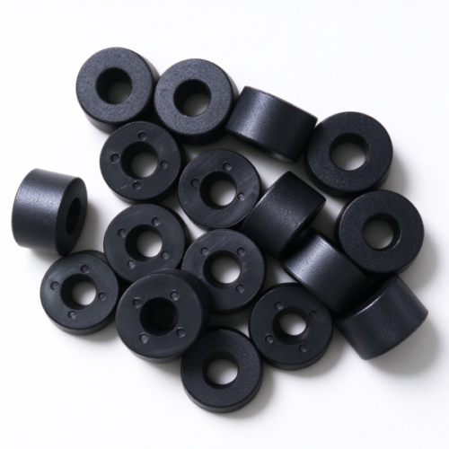 Molded plastic spacer rings in black, a pile of rings with center bores and small holes around the bore