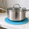 Silicone honeycomb mat in light blue with a steel pot standing on it on a kitchen counter